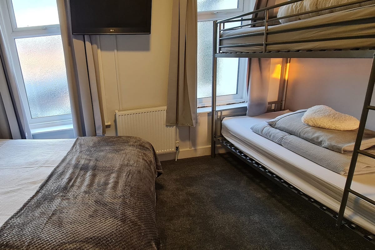 A hotel room with a bed, a bunk bed, a TV, and a window with curtains.