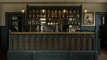 A bar area with a dark wooden counter, multiple bottles, and a vintage-style light fixture.