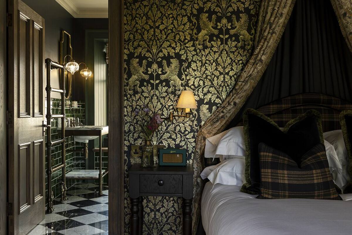 A bedroom with a bed, a nightstand, a lamp, and a mirror. There is a bathroom visible through an open door.