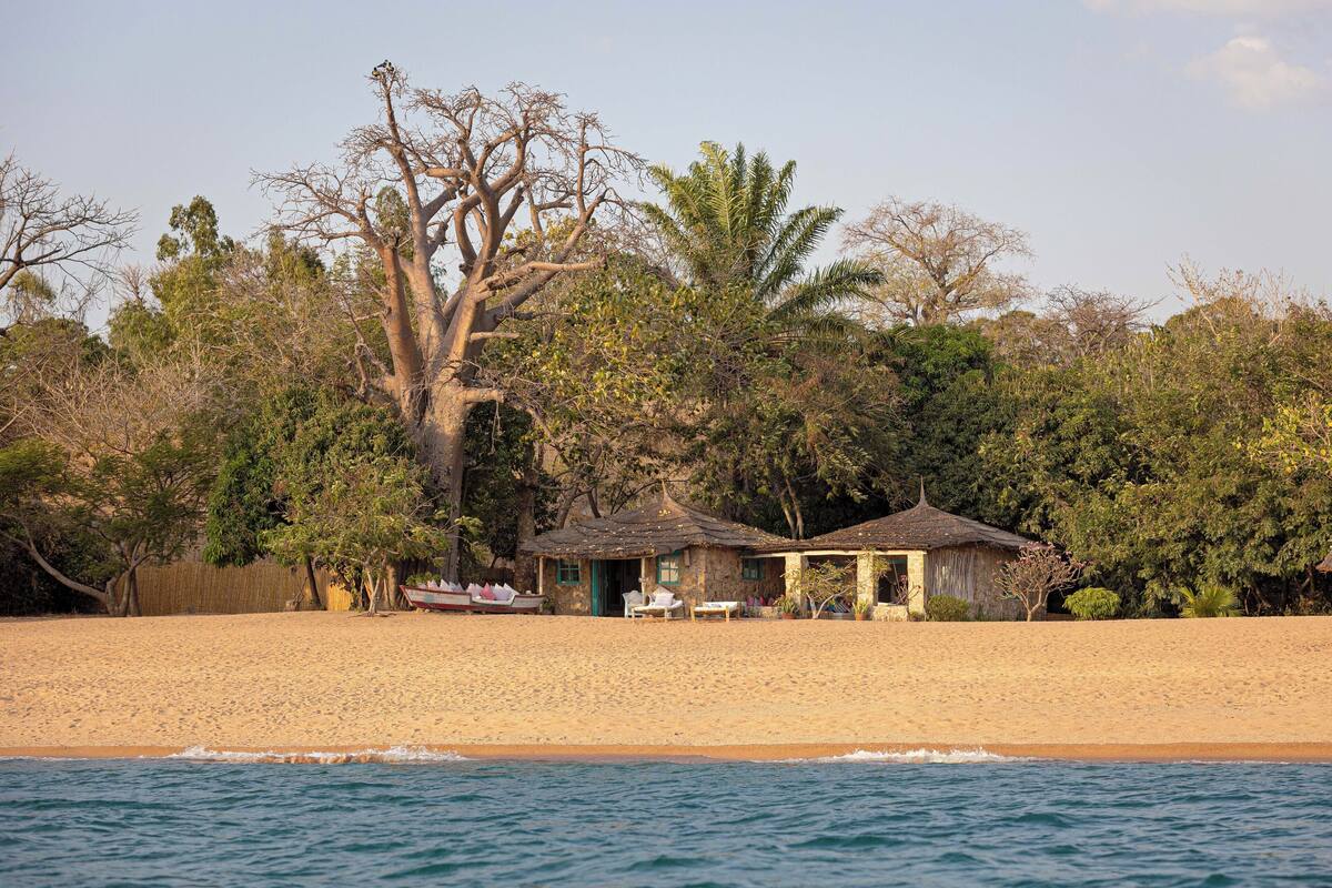 A beach house with a thatched roof, surrounded by trees and a sandy beach.