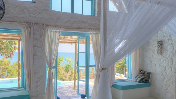A bedroom with a large bed, a window with a view of the ocean, and a thatched roof. - Kaya Mawa (Likoma Island)