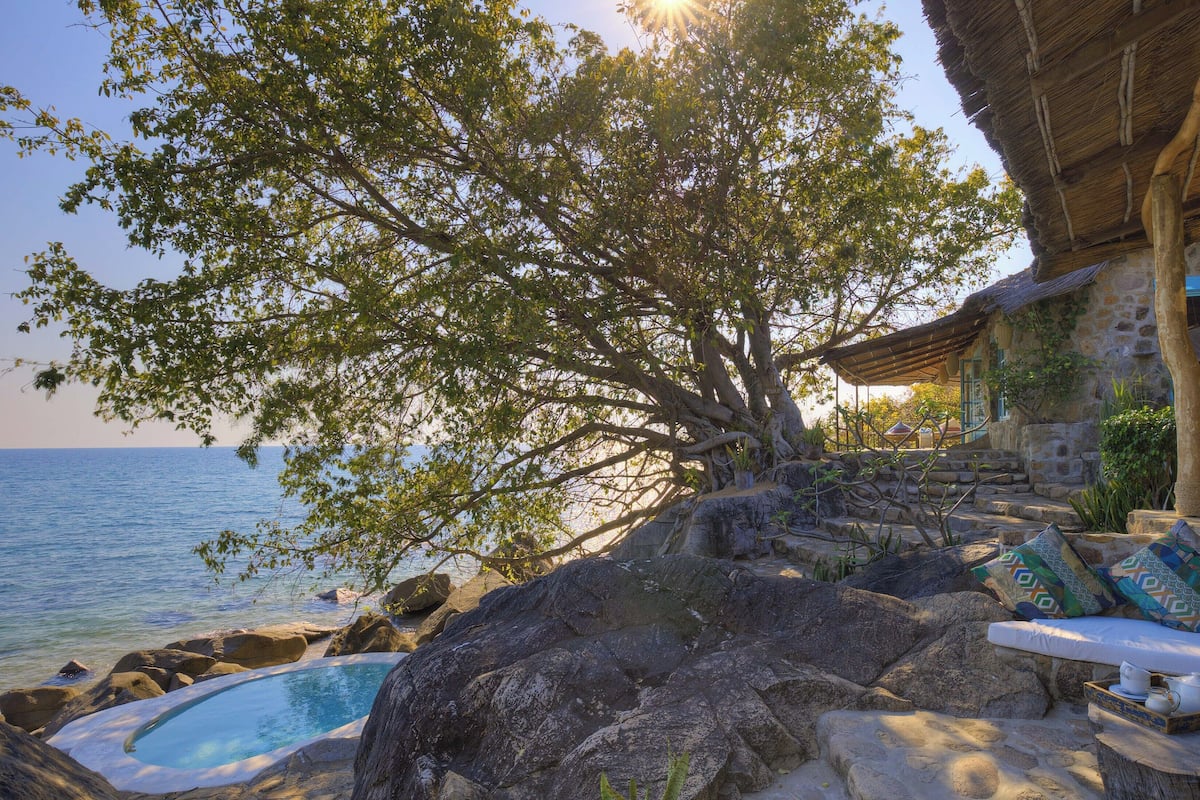 A stone building with a thatched roof, a pool, and a view of the sea.