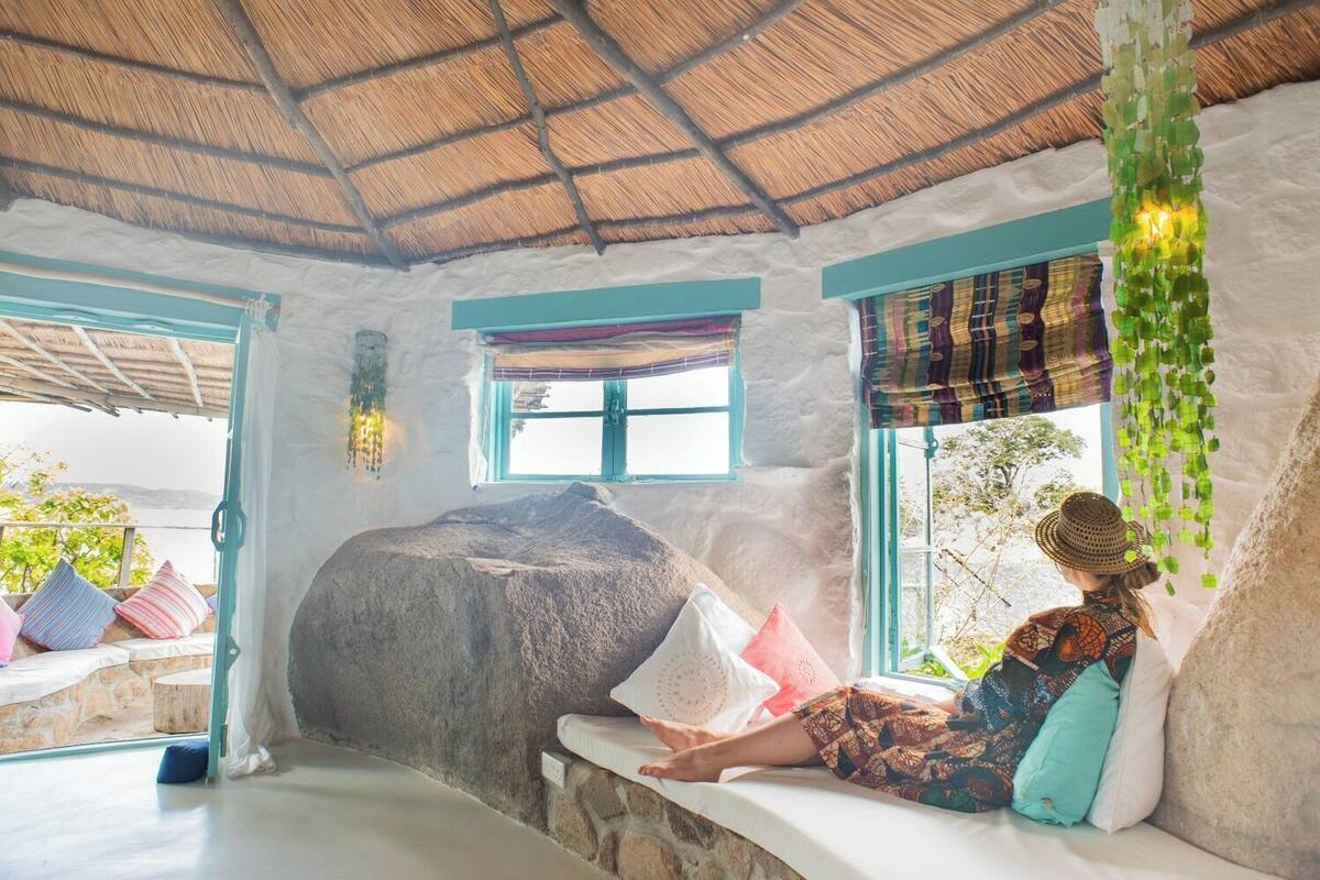 A room with a stone wall, a window with a colorful curtain, and a hanging plant.