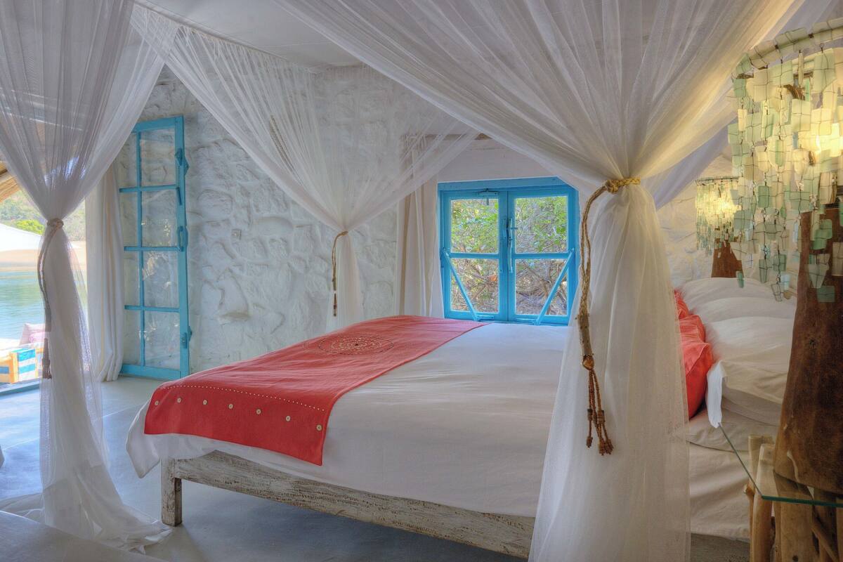 A bedroom with a bed, a window, and a view of the sea.