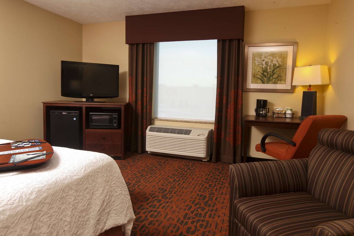 A hotel room with a bed, a TV, an air conditioner, a coffee maker, and a framed picture on the wall.