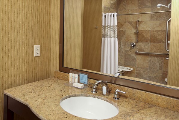 A bathroom with a granite countertop, a white sink, a mirror, and a shower area with a glass door.