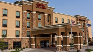 A Hampton Inn & Suites hotel with a modern design, featuring a stone facade, multiple windows, and an American flag.