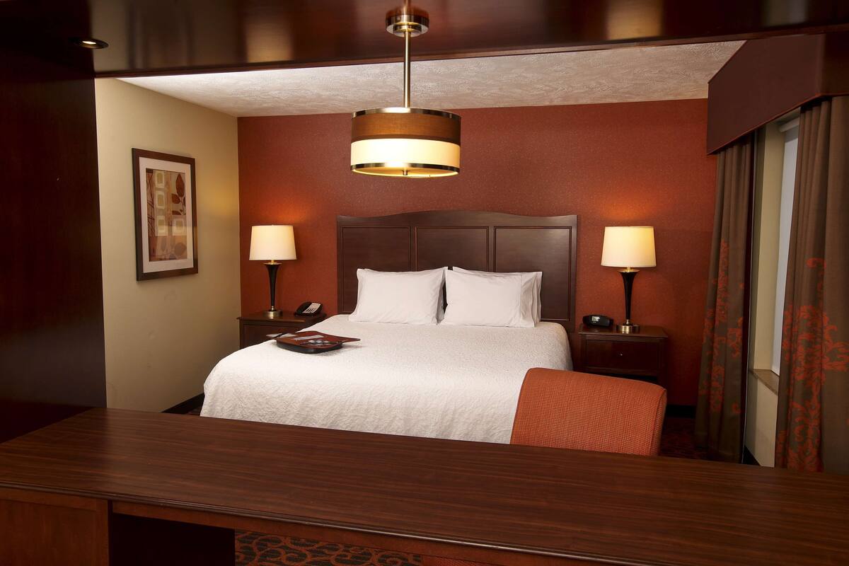 A hotel room with a large bed, two bedside tables with lamps, a wooden desk, and a framed picture on the wall.
