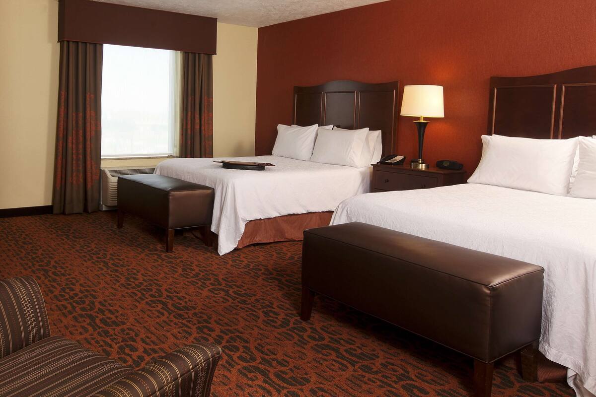 A hotel room with two beds, a desk, a chair, and a sofa.