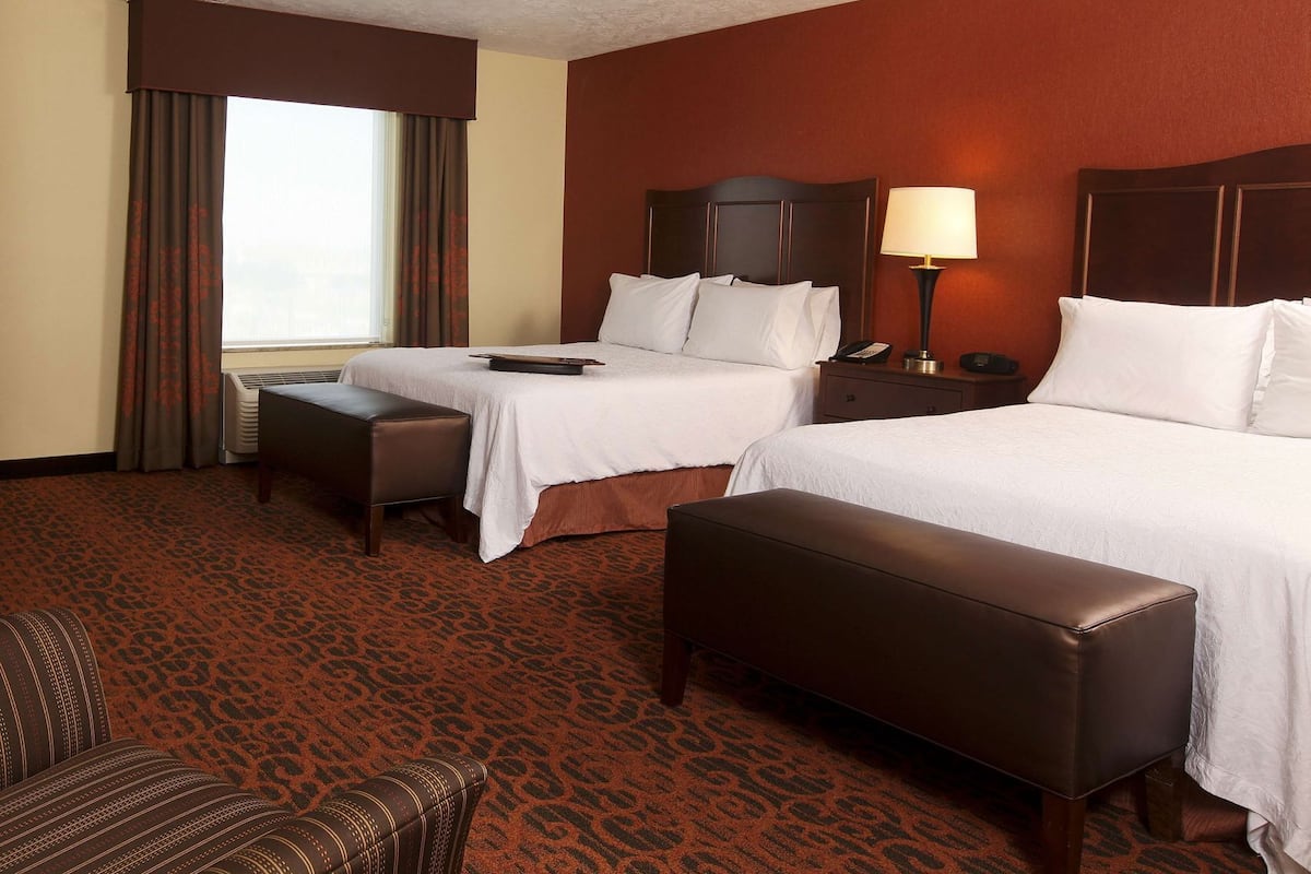 Ein Hotelzimmer mit zwei Betten, einem Schreibtisch, einem Stuhl und einem großen Fenster mit Vorhängen.