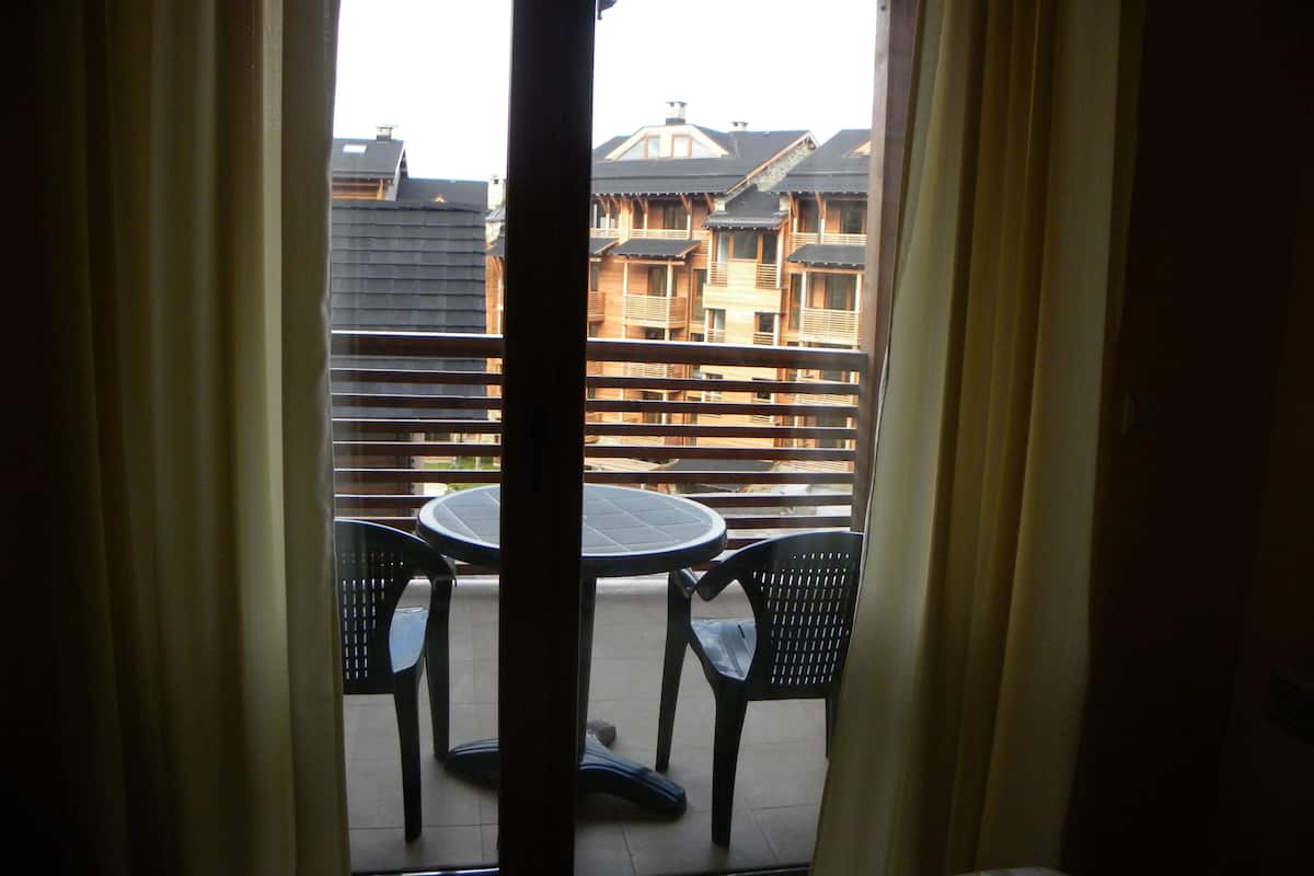 A balcony with a table and chairs, a view of buildings, and curtains.