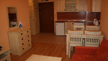 Une cuisine compacte avec des meubles en bois, un petit réfrigérateur et un coin repas comprenant une table et des chaises.