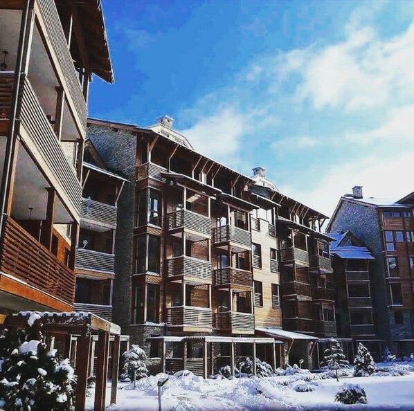 A multi-story building with balconies, a covered entrance, and snow-covered surroundings. - St. Ivan Ski Resort (Bansko)