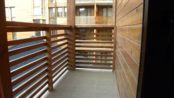 Un balcon étroit doté de balustrades en bois, d’un sol carrelé et offrant une vue sur un immeuble à plusieurs étages avec des fenêtres.