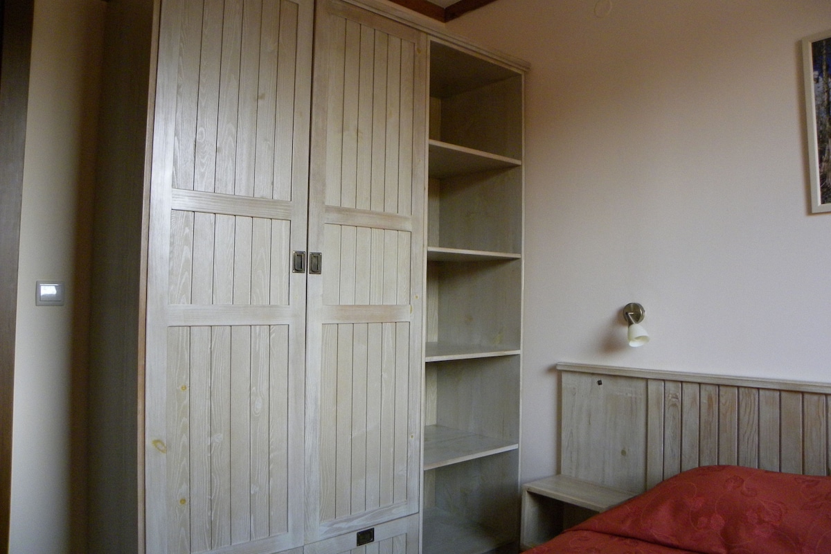 A room with a large wardrobe, a bed, and a small bedside table.