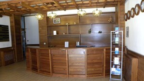Un comptoir d’accueil en bois, un sol carrelé, des étagères en bois ornées de tableaux encadrés et une échelle pour ranger les livres.
