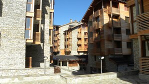 Un immeuble à plusieurs étages, avec une façade en pierre et en bois, des balcons et une cour pavée de pierres.