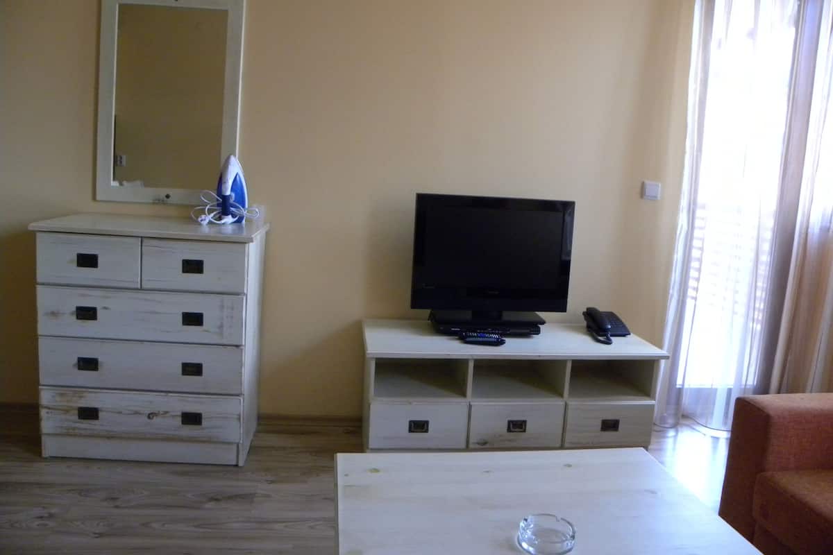 A room with a television on a stand, a dresser with multiple drawers, a small table, and a chair.