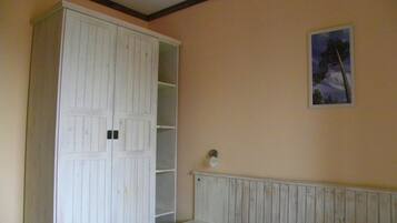 Une chambre avec une grande armoire blanche, un lit et une petite table de chevet.