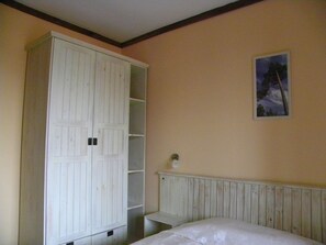 A bedroom with a large white wardrobe, a bed, and a small bedside table.