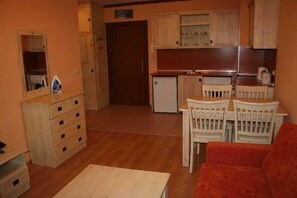 A compact kitchen with a refrigerator, a dining table with chairs, a sofa, and a wooden dresser with drawers. - St. Ivan Ski Resort (Bansko)