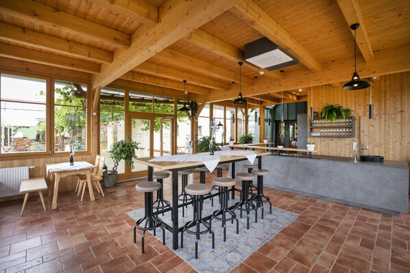 A spacious kitchen with wooden beams, a long bar area with stools, and large windows allowing natural light.