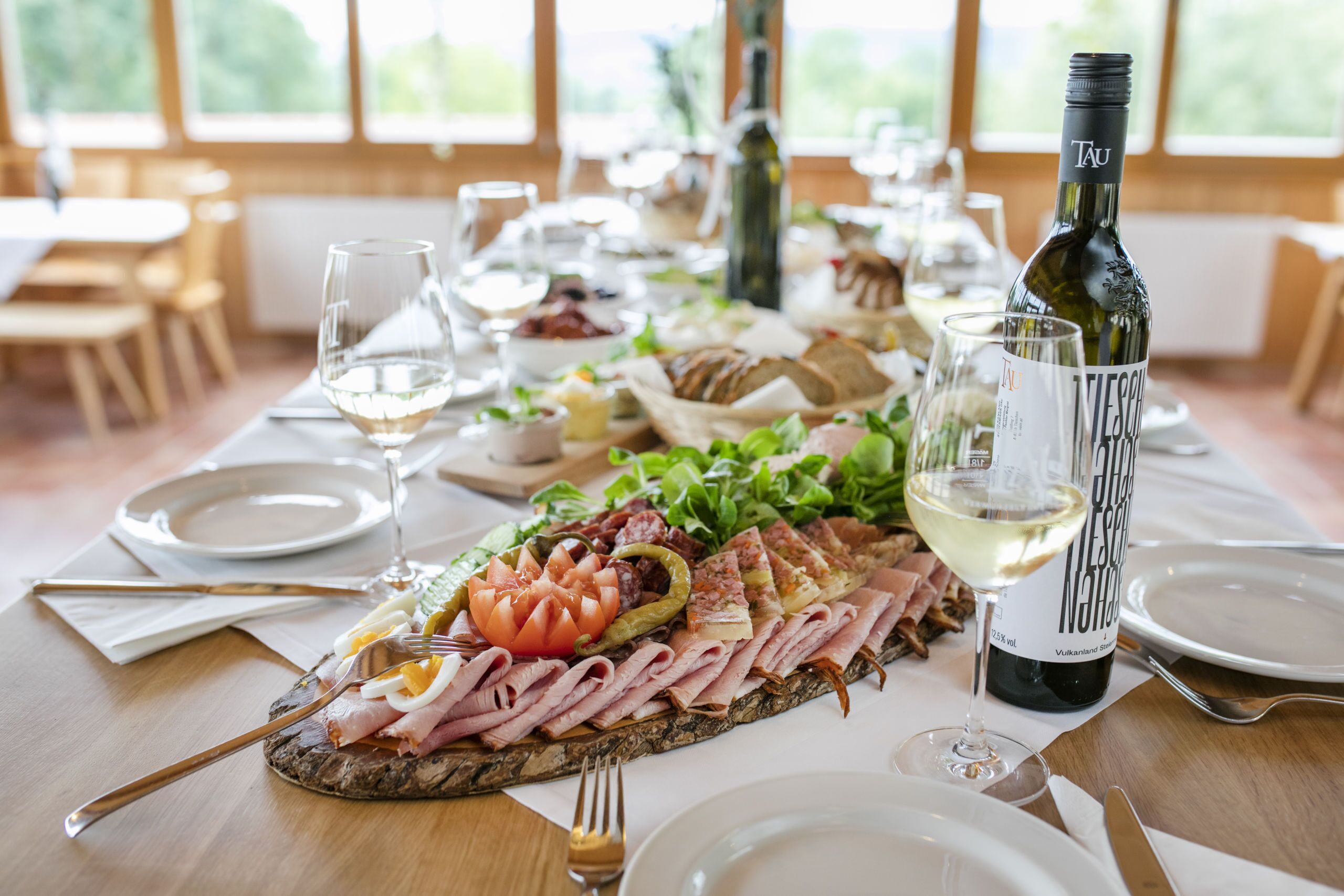 A table set for a meal with a variety of food items, including meats, vegetables, and a bottle of wine.