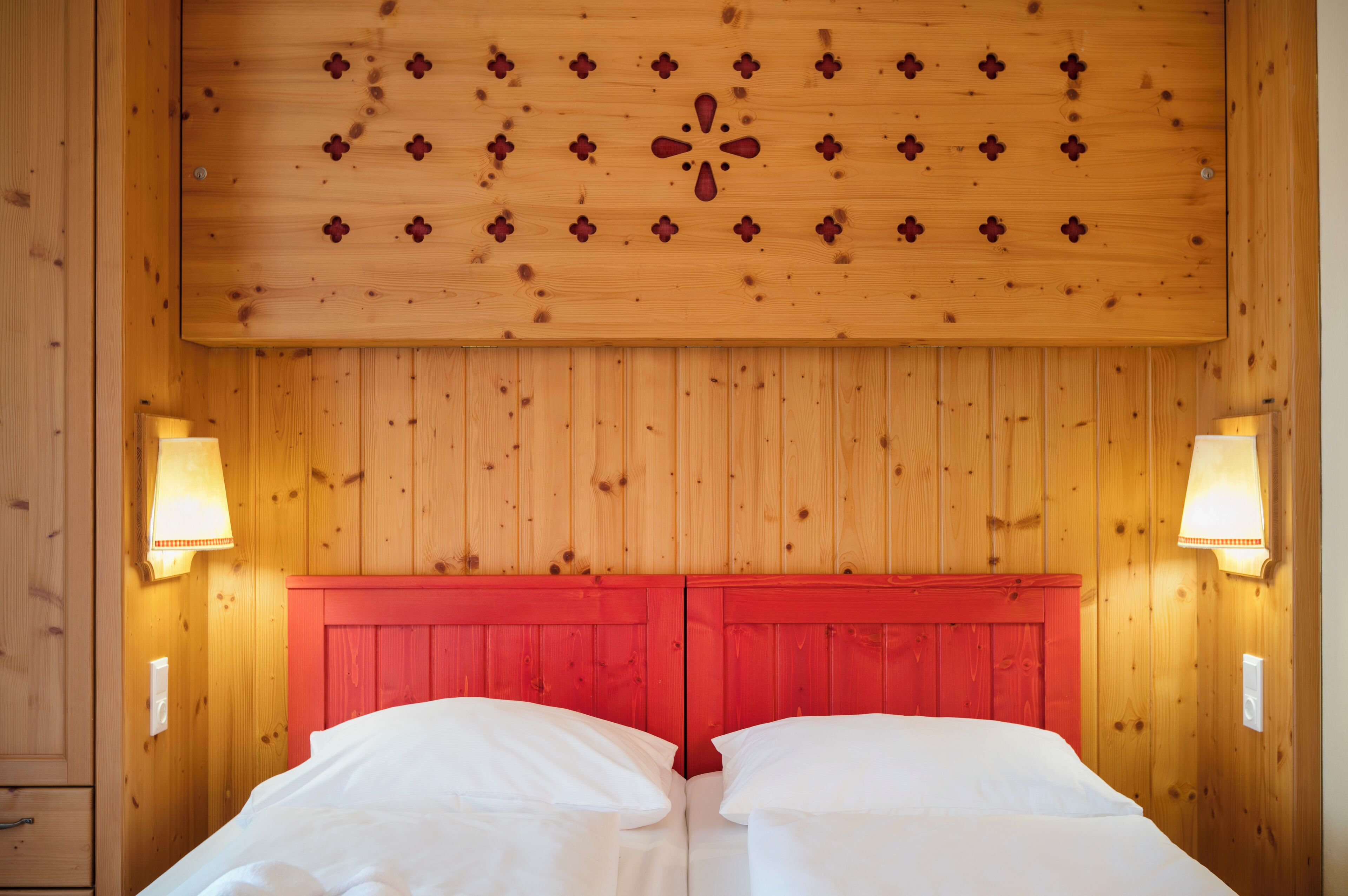 A room with wooden panel walls, a red headboard, two bedside lamps, and a bed with white linens.