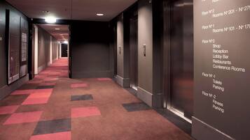 Et hotel med rødt tæppe, elevator og en opslagstavle med værelsesnumre og faciliteter.