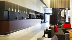 A modern hotel lobby with a reception desk, seating area, and a staircase.