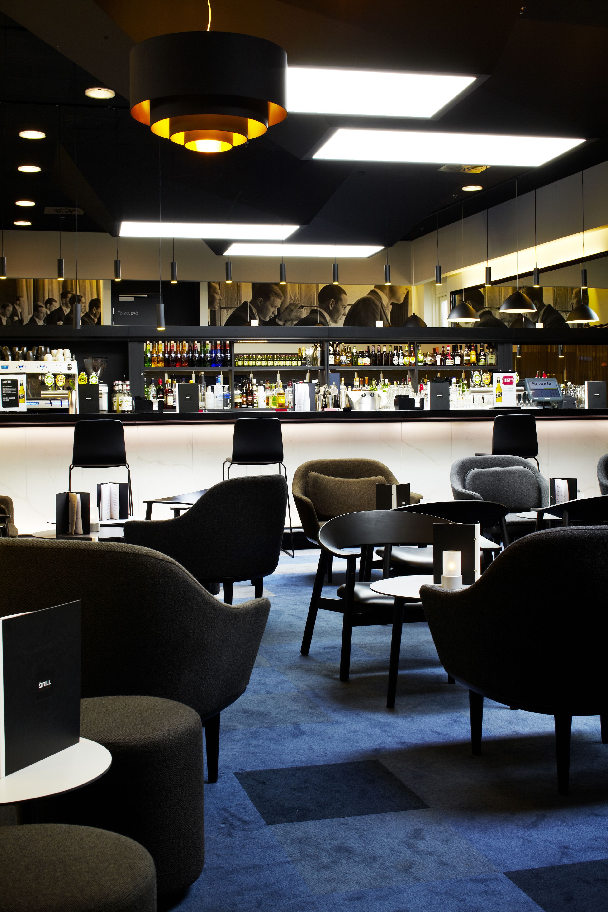 A bar area with seating, a counter with various bottles, and overhead lighting.