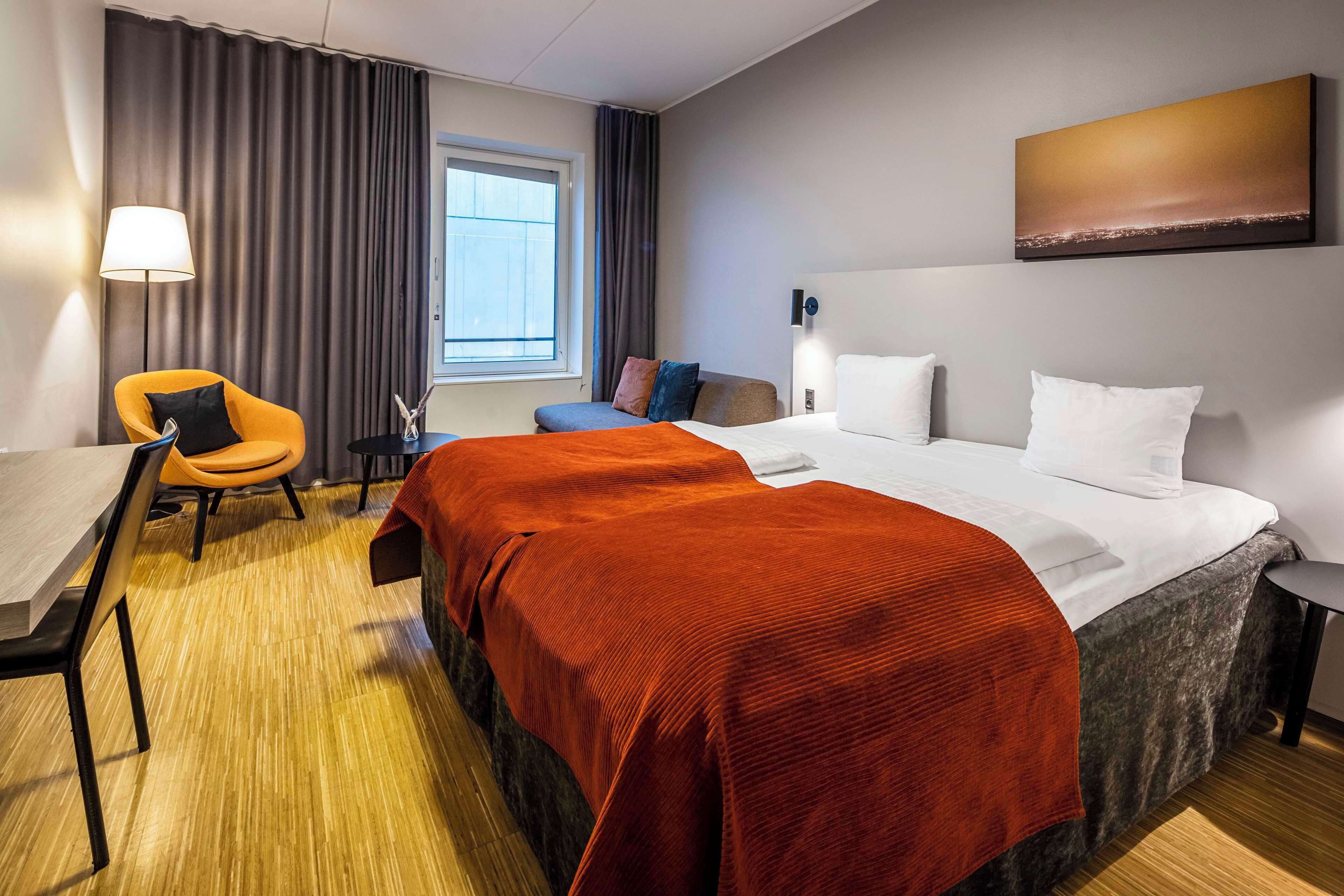 A hotel room with a bed, a desk, a chair, and a window.
