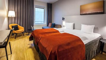 A hotel room with a bed, a desk, a chair, and a window.