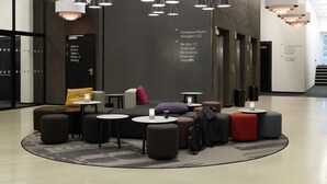 A modern lobby with seating areas, a staircase, and directional signs for conference rooms and restrooms.