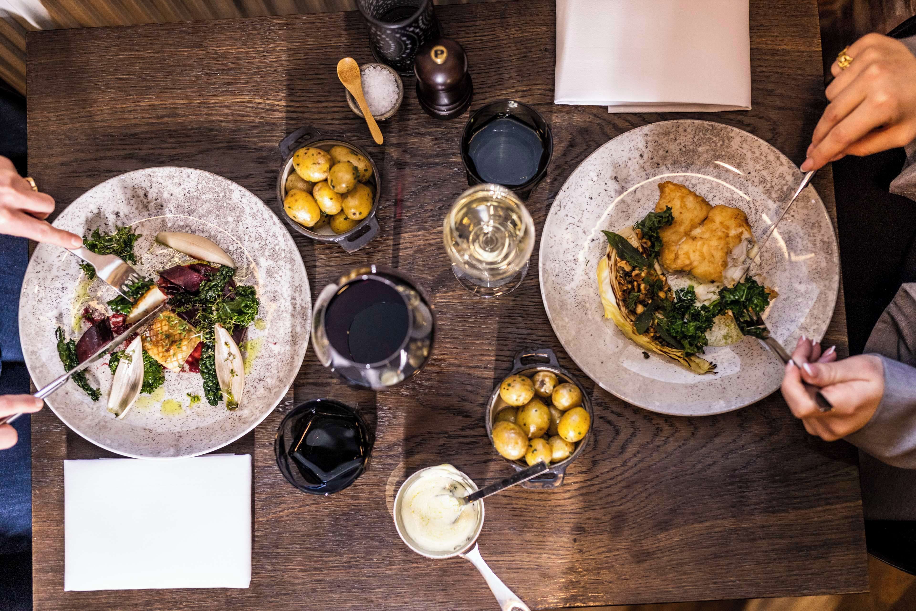 Una mesa de comedor con platos de comida, copas de vino y salero y pimentero.