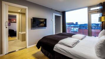 Quarto de hotel com cama, televisão, porta para uma varanda e vista para a cidade.