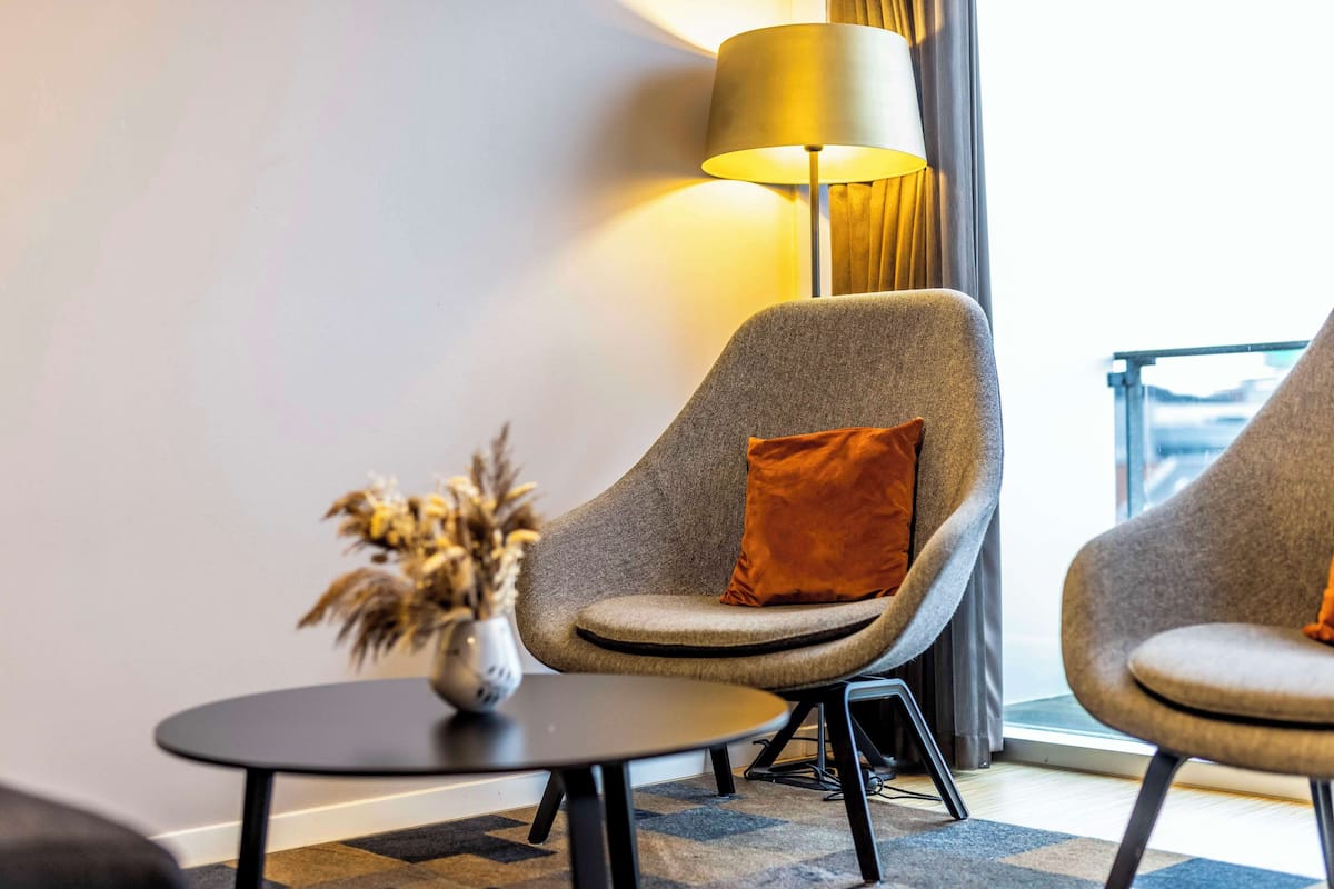 A modern room with two grey armchairs, a small round table, and a floor lamp.