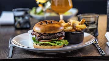 Egy tányér, rajta egy hamburger, sült krumpli és egy pohár sör, egy faasztalon.