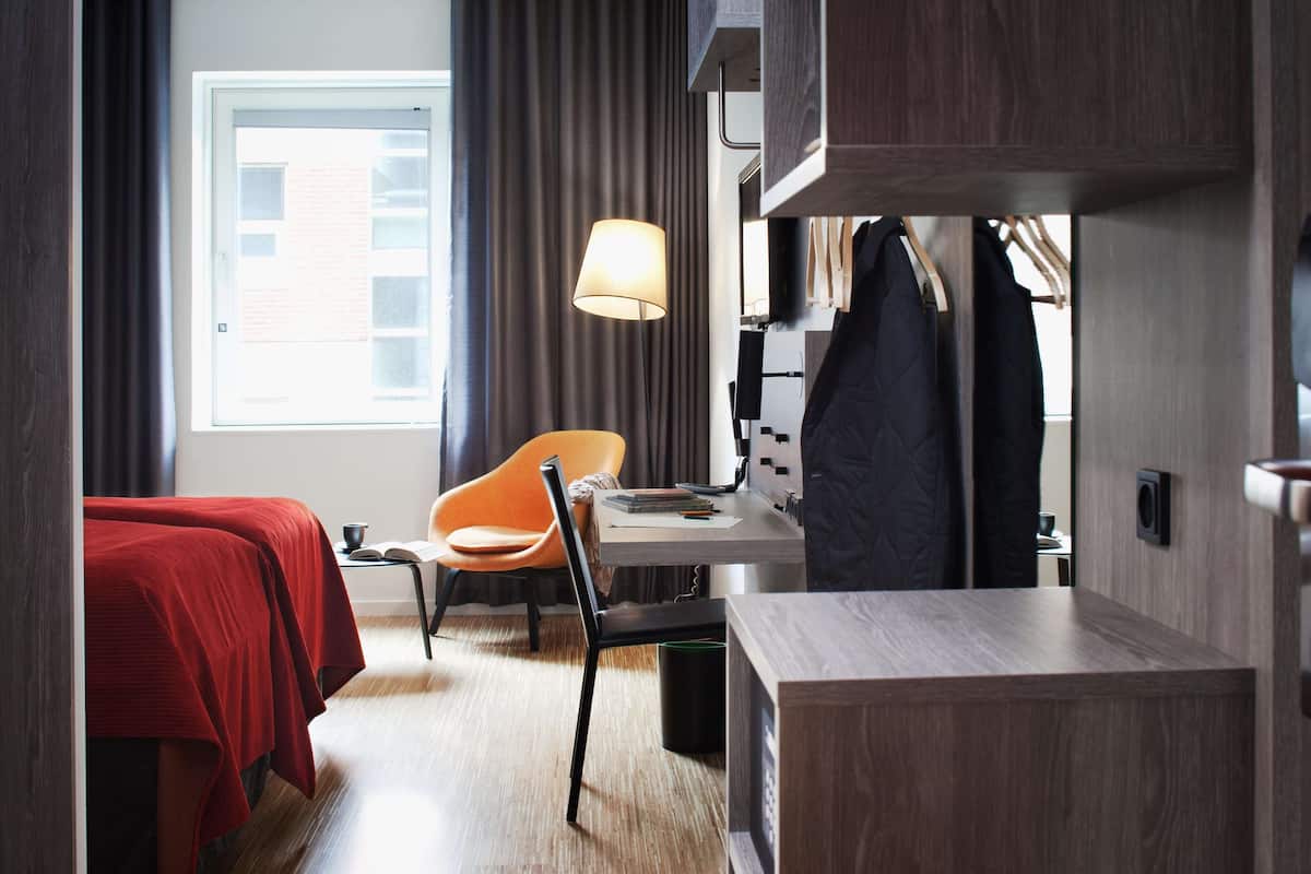 A hotel room with two beds, a desk, a chair, a lamp, and a wardrobe.