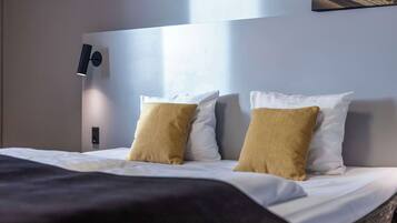 A neatly made bed with white and mustard-colored pillows, a black headboard, and a wall-mounted light fixture.