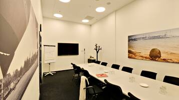 A conference room with a long table, black chairs, a whiteboard, and a large painting of a river scene.