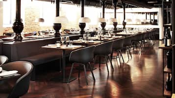A restaurant with long tables, black chairs, and hanging lamps.