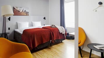 A hotel room with a bed, a chair, a small table, a lamp, and a painting on the wall.