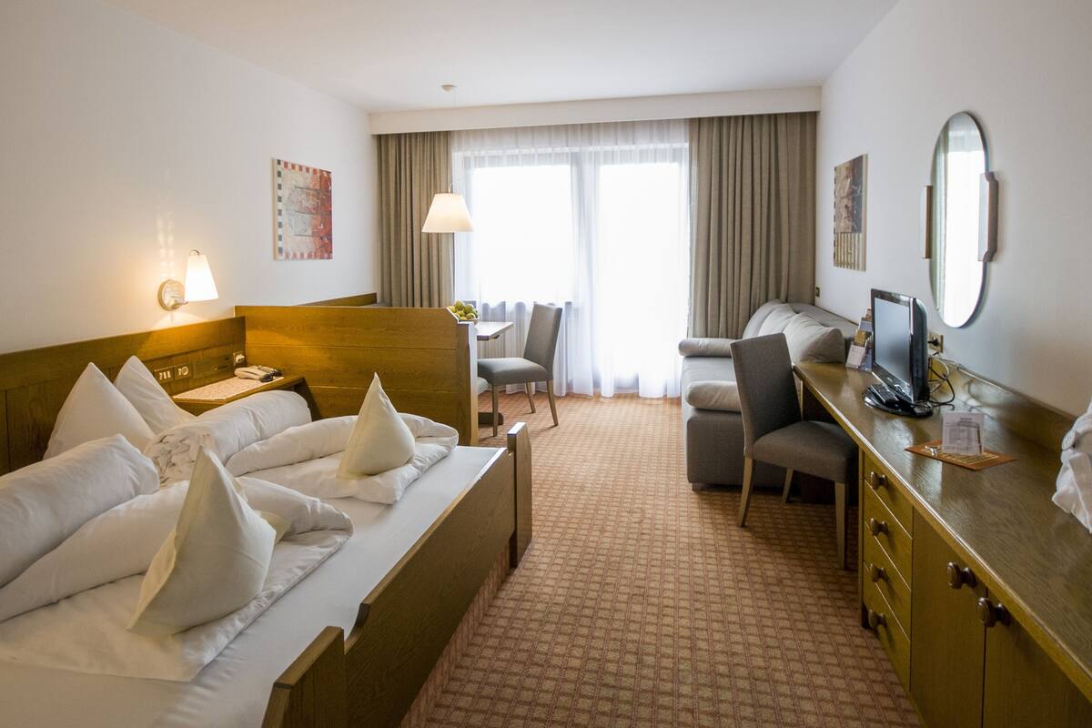 A hotel room with a bed, a desk, a chair, a TV, and a bathroom area.