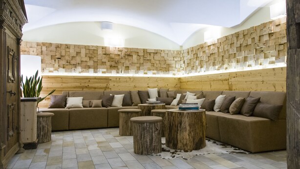 A cozy living area with a wooden wall, a sofa, and round wooden tables. - Christophs Hotel (Schenna)