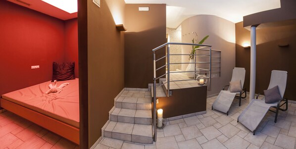 A hotel room with a bed, a small staircase, a seating area with chairs, and a plant.