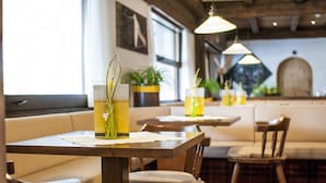 A restaurant interior with wooden tables and chairs, potted plants, and hanging pendant lights. - Christophs Hotel (Schenna)