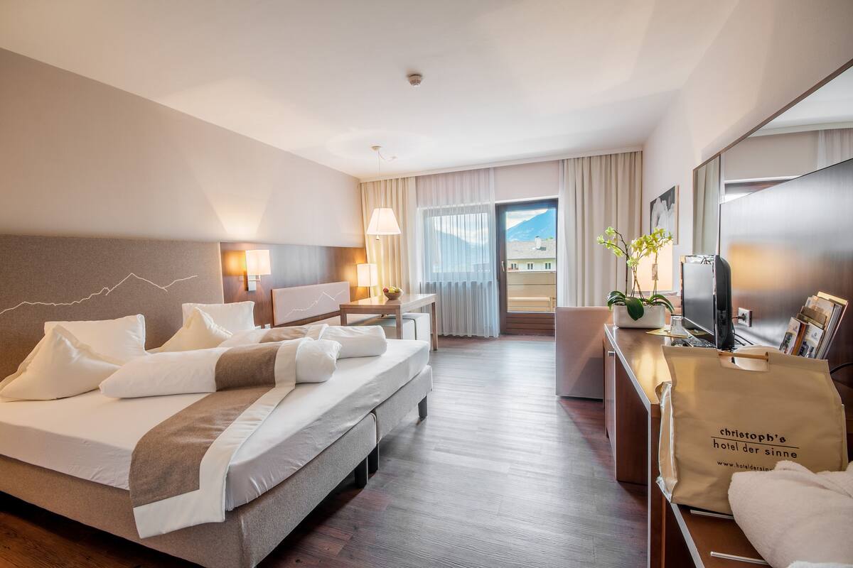 A hotel room with a bed, desk, chair, lamp, and a view of the outdoors.