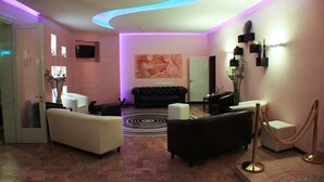 A modern lobby with a curved ceiling, a black sofa, a white sofa, a black armchair, and a reception desk. - Hotel Julia (Comacchio)