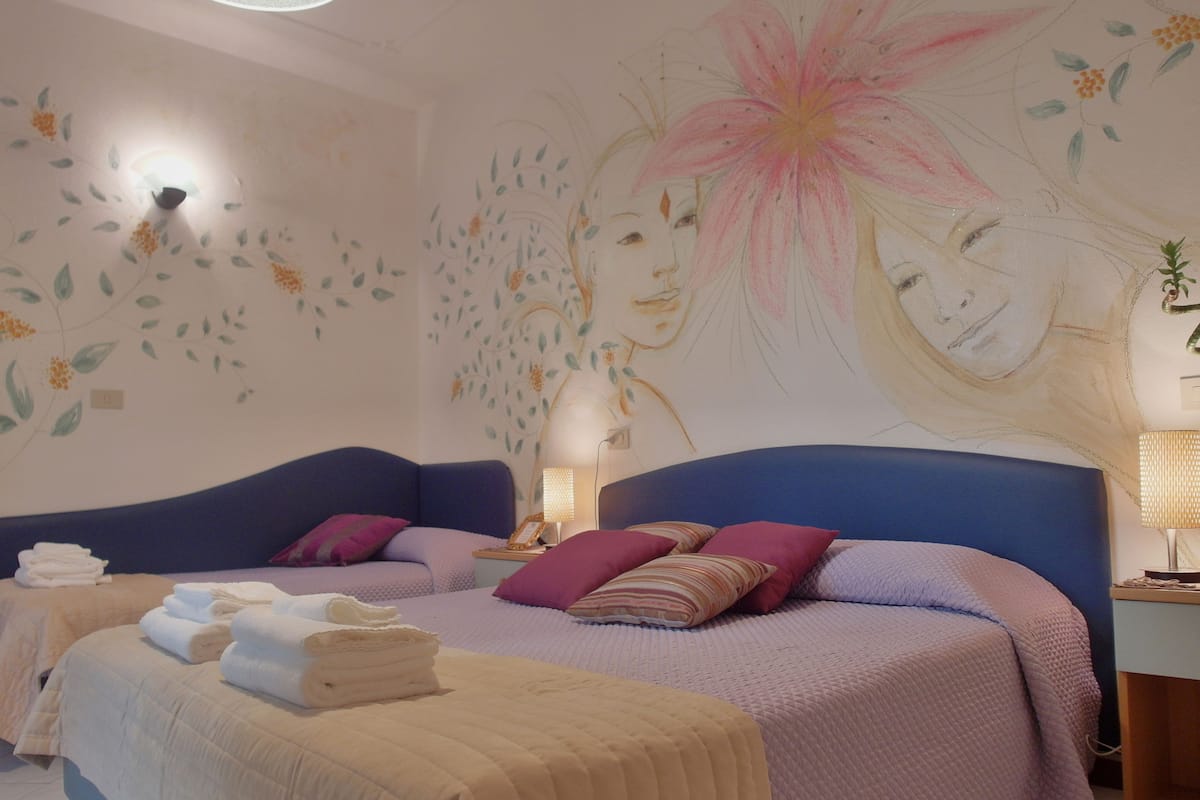 A bedroom with a large bed, two bedside tables, a wall mural, and a ceiling light.